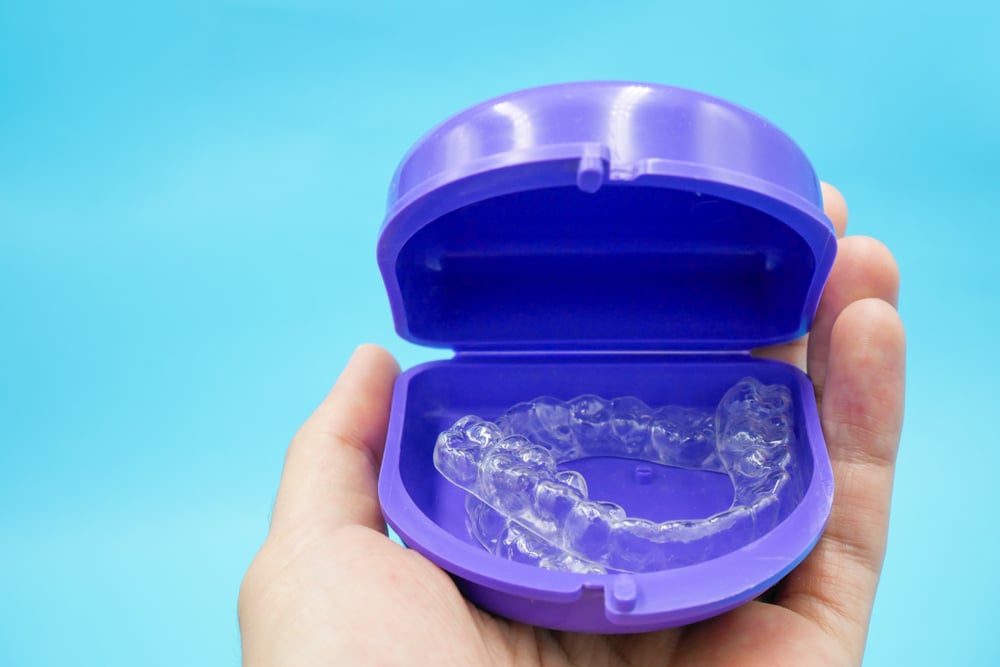 Someone holding a set of clear aligners in their case to protect them and ensure they stay clean. Someone holding a set of clear aligners in their case to protect them and ensure they stay clean.