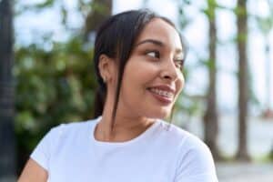 Adult woman wearing a white shirt smiles outdoors, revealing braces on her teeth